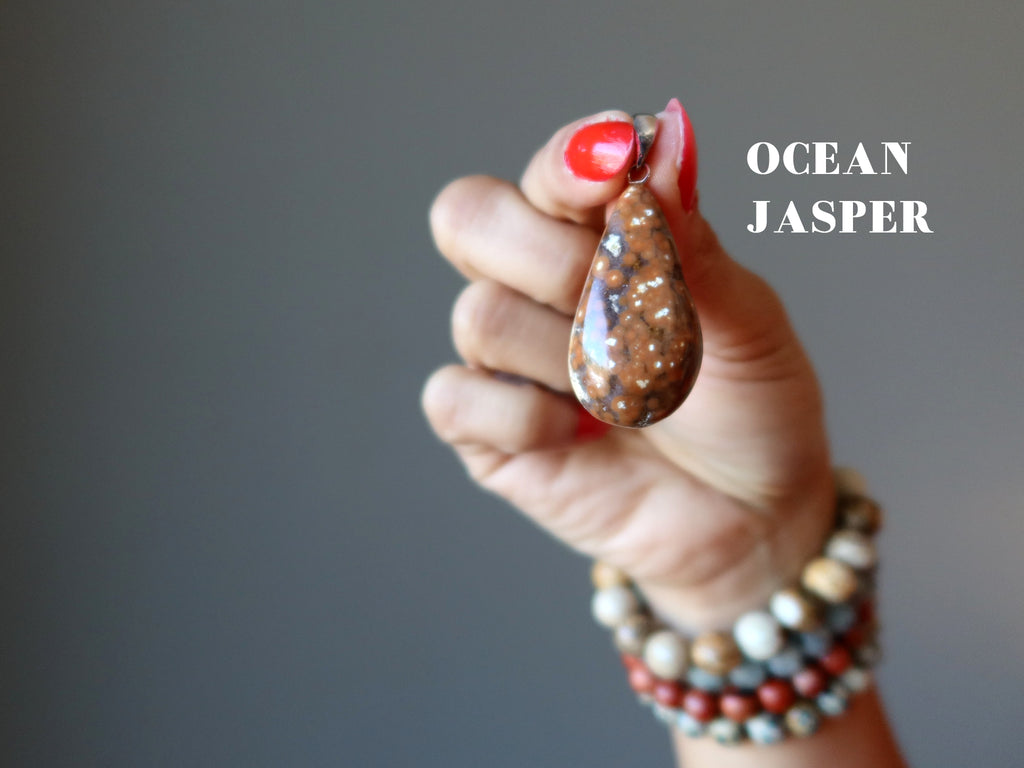 hand wearing jasper bracelets holding a ocean jasper teardrop pendant