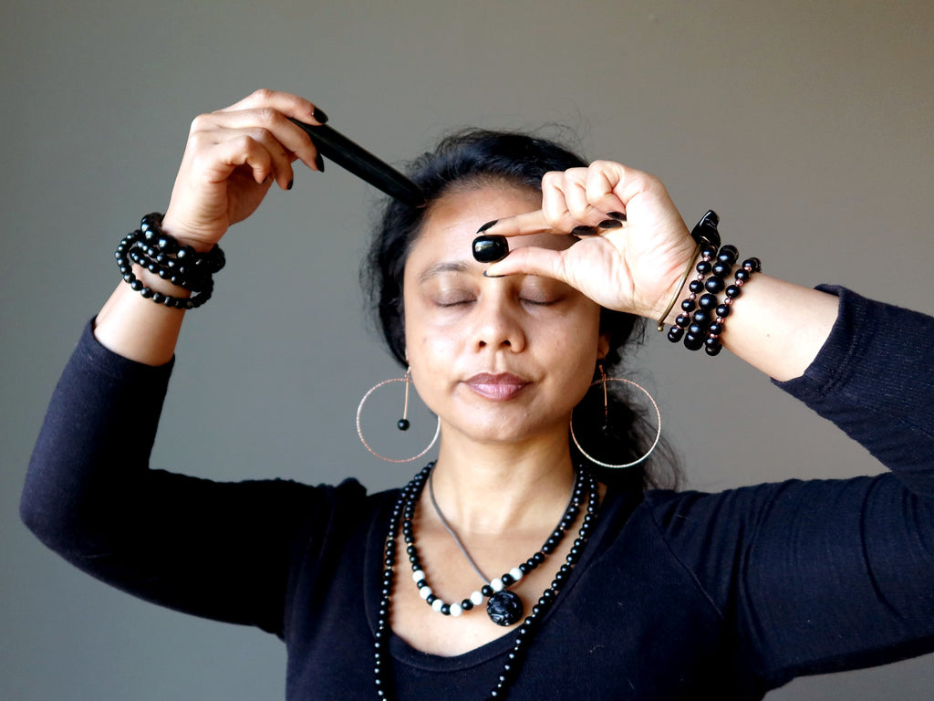 woman holding jet tumbled stone and wand to third eye