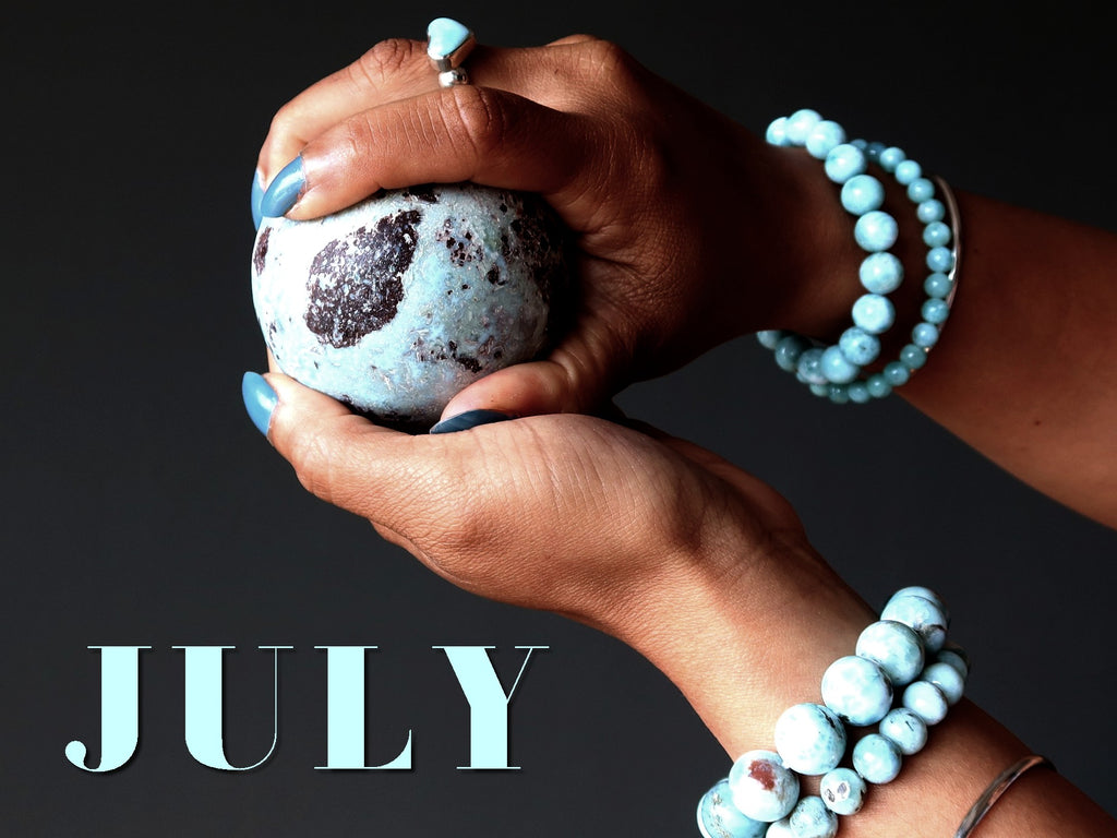 hands holding larimar sphere wearing larimar jewelry with word JULY