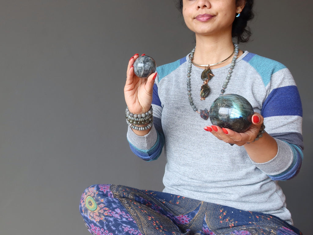 female sitting cross legged holding labradorite spheres