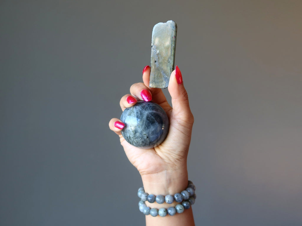 hand wearing labradorite bracelets holding a labradorite sphere and polished stone