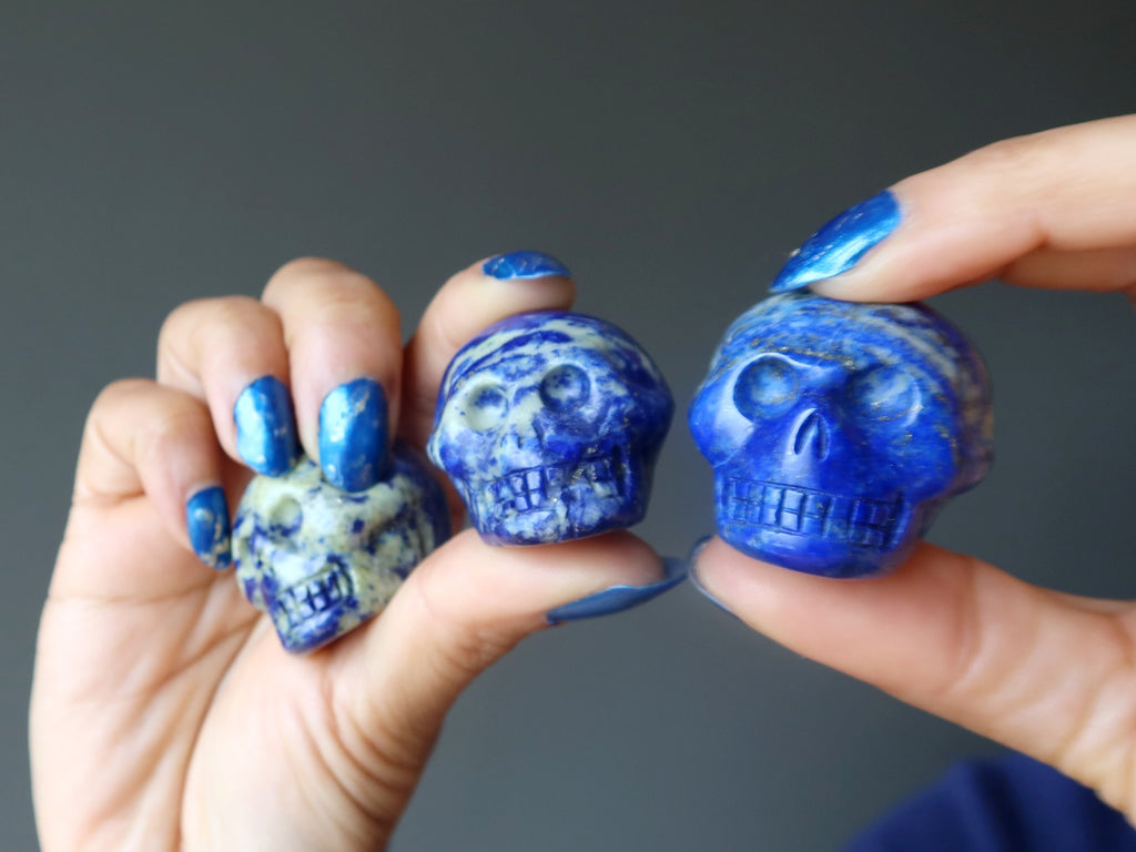 hands holding up three lapis lazuli skull figurines