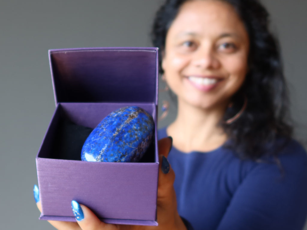 sheila of satin crystals holding a purple gift box with a lapis lazuli polished gemstone