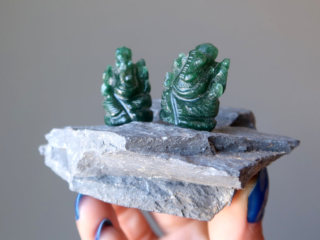 two dark green aventurine ganesh figurines on a gray rock
