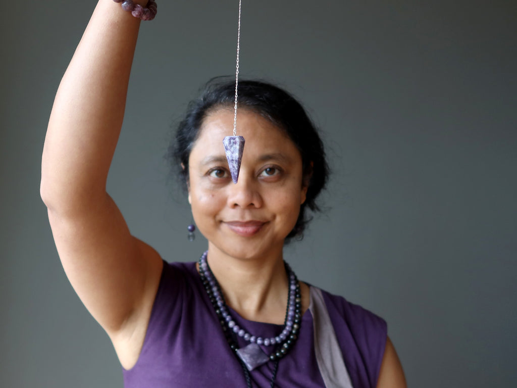 woman with lepidolite pendulum at third eye chakra