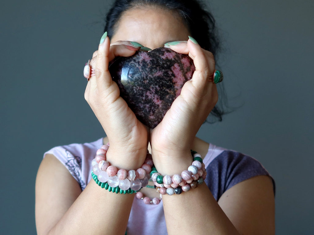 woman holding rhodonite heart wearing malachite and rhodochrosite and rose quartz jewelry