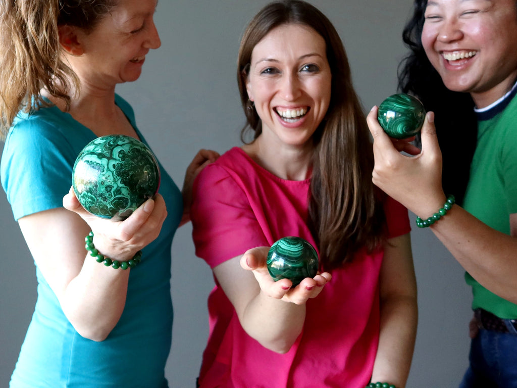 three females laughing holding malachite crystal spheres