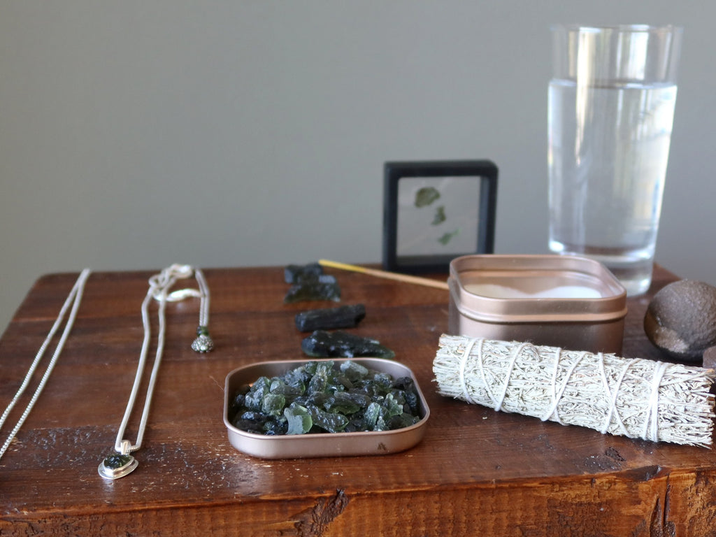 moldavite stones and jewelry with sage, incense, candle, moqui marbles and water