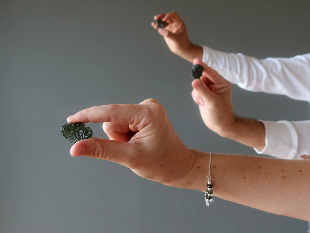 three hands holding raw moldavite