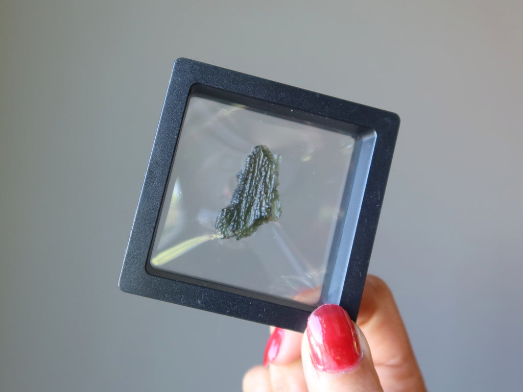 hand holding up a raw green moldavite in clear suspension display case
