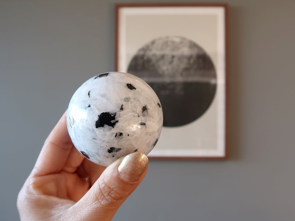 hand holding rainbow moonstone tourmaline sphere in front of a moon picture