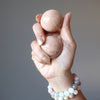 hand wearing moonstone bracelets holding two peach moonstone spheres