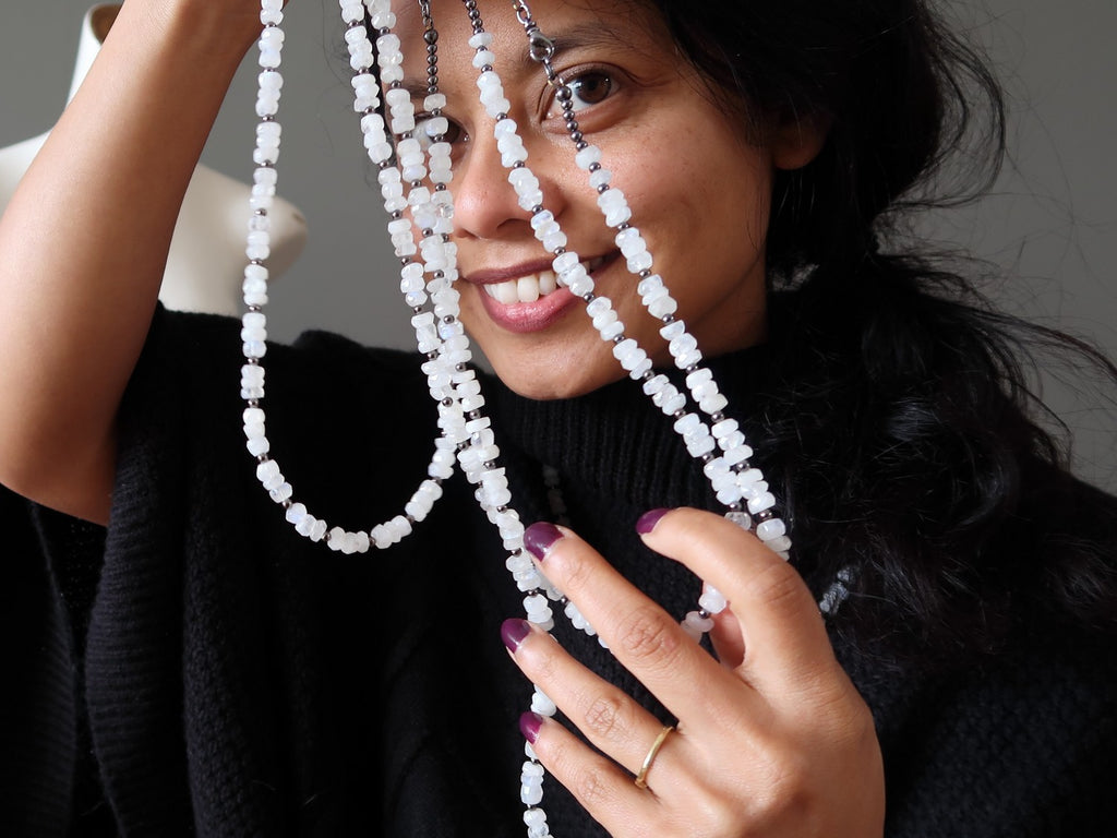 Satin Crystals jewelry designer with 3 strands of white Rainbow Moonstone necklaces in front of her face.