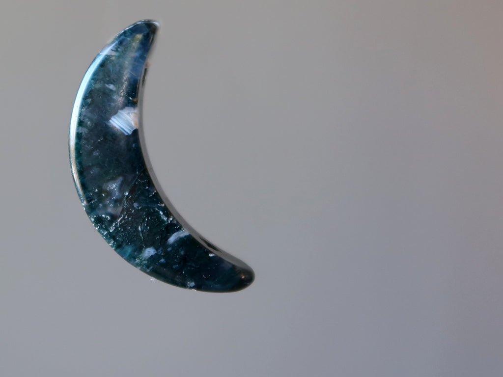 green and white moss agate crescent moon stone on gray background