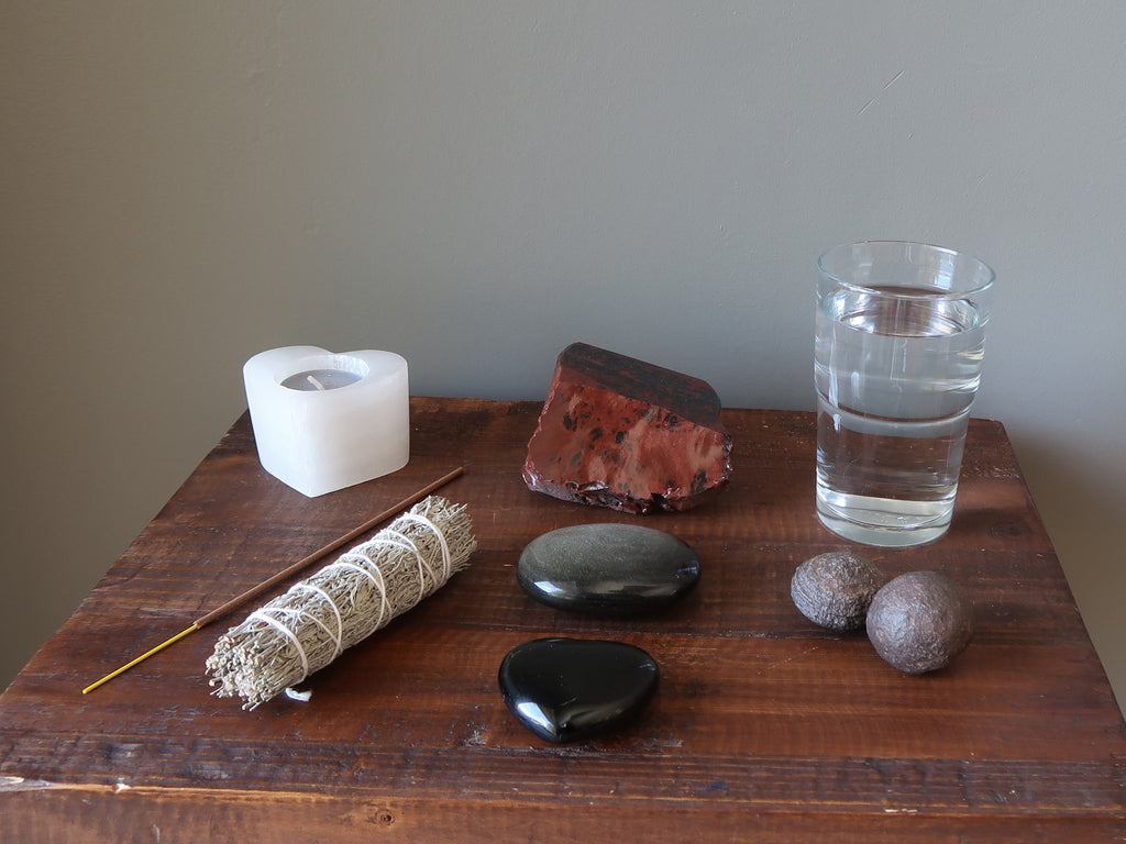 candle, incense, sage, obsidian stones, glass of water and moqui marbles on a table