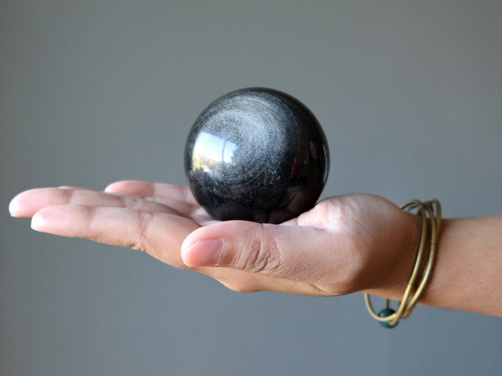 hand holding a silver sheen obsidian sphere