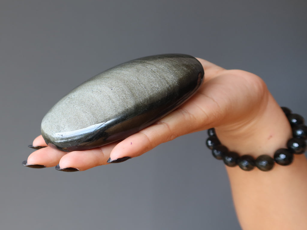 hand holding a large oval sheen obsidian palm stone