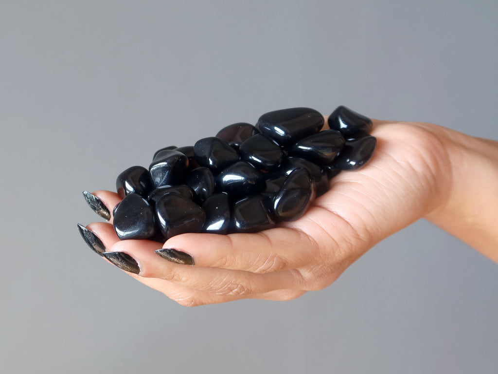 hand holding a pile of black obsidian tumbled stones