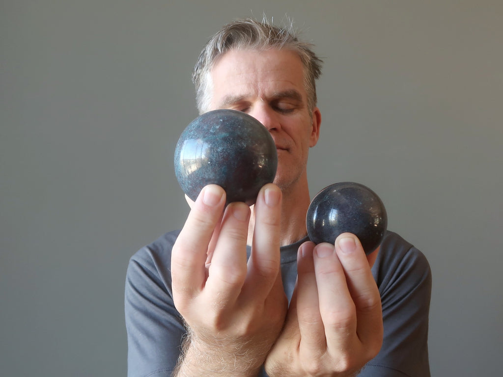 man with eyes closed holding two ruby kyanite spheres