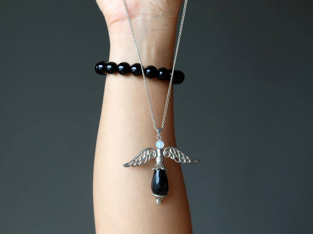 hand wearing black onyx bracelet holding onyx angel necklace