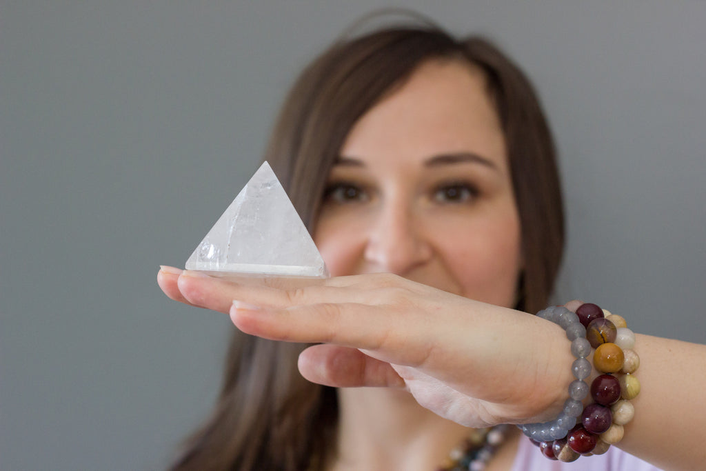 clear quartz pyramid balanced on back of female's hand in foreground of brunette's head against gray wall