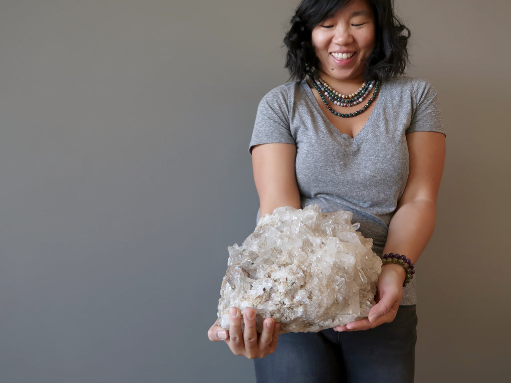 Large Quartz cluster held by female mode against gray background at Satin Crystals Shop