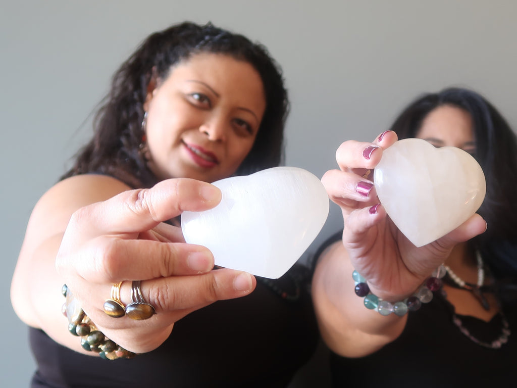 Two girls holding out white Selenite and snow Quartz polished stone heards at Satin Crystals Boutique.