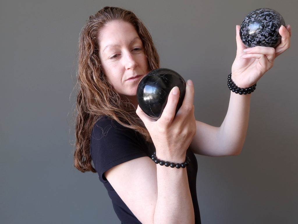 jamie of satin crystals holding up a black tourmaline and gabbro stone sphere for protection