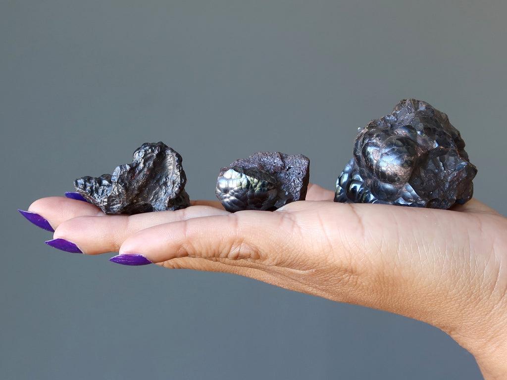 hand holding three raw hematite stones