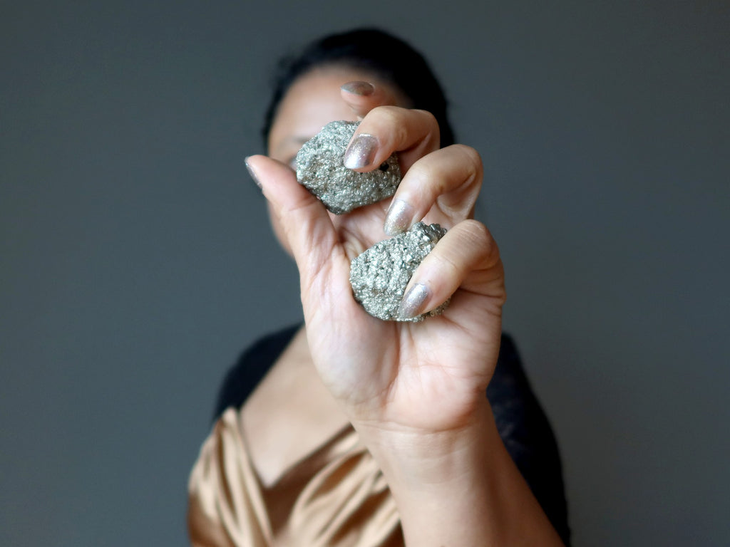 female holding two raw pyrite stones in her hand