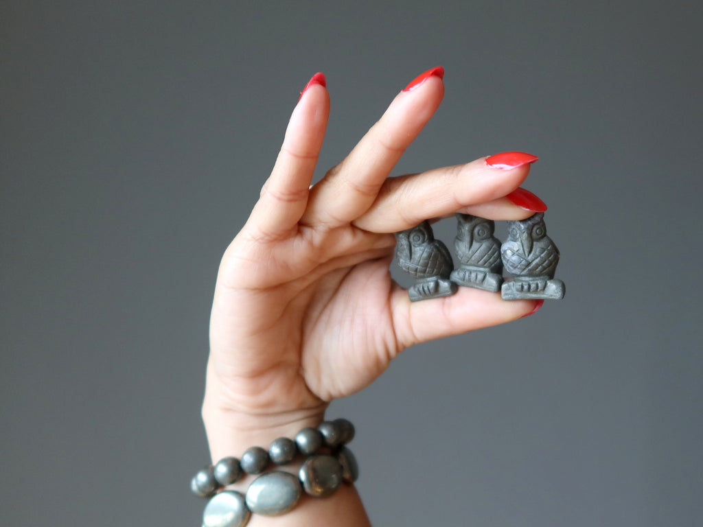 hand wearing pyrite bracelets holding three pyrite owl carvings