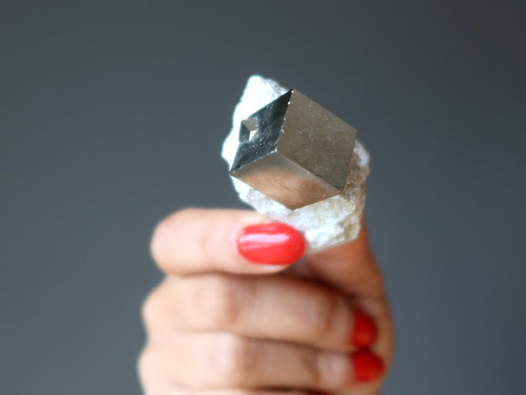hand holding pyrite cube in white matrix