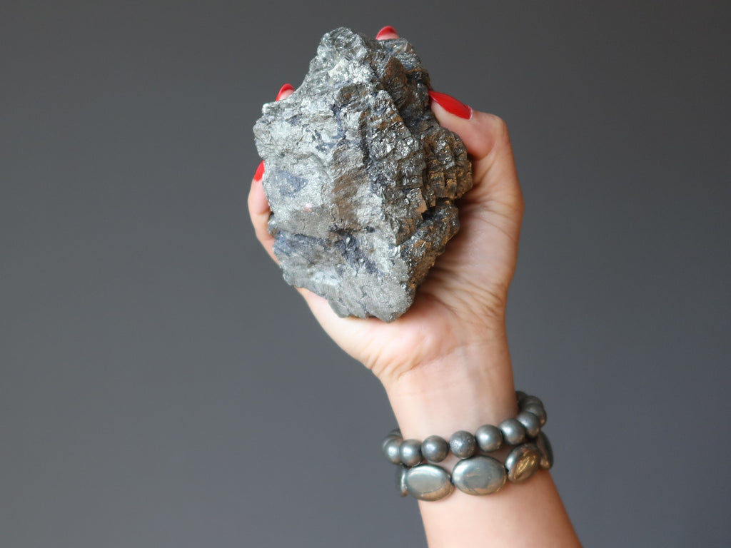 hand wearing pyrite bracelets carrying a pyrite cluster