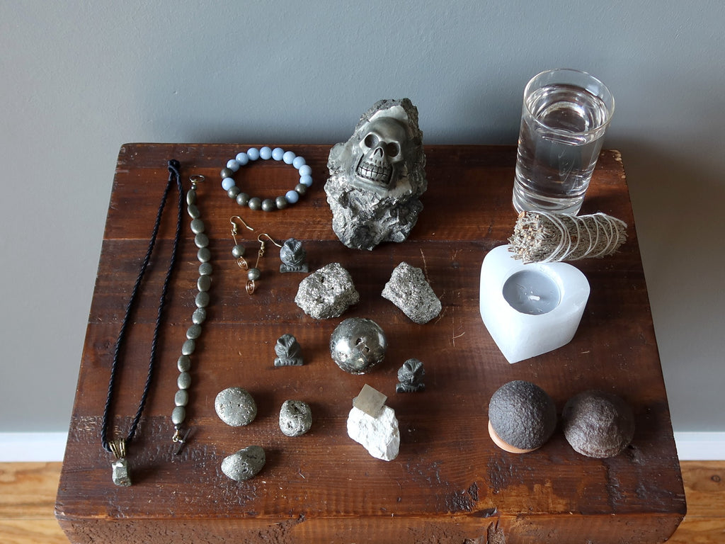 a wood table with pyrite jewelry, stones, water, candle, sage, and moqui marbles
