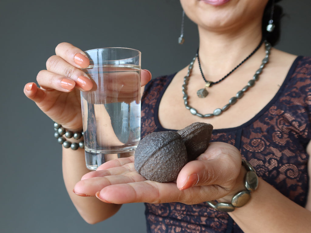female holding glass of water and pair of moqui marble stones