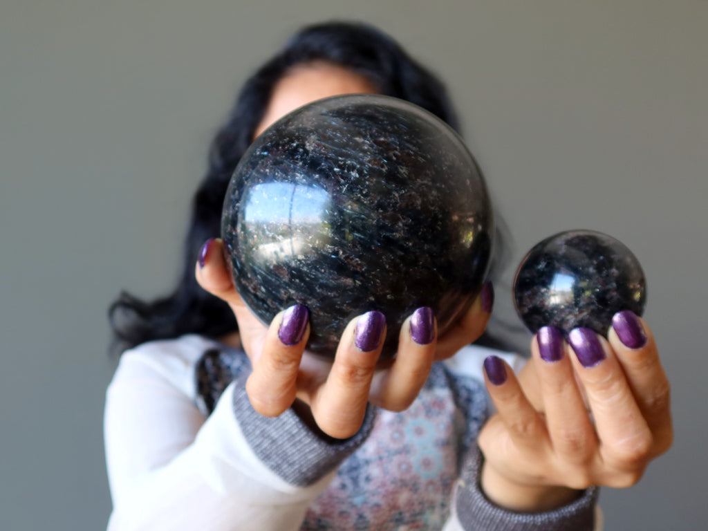 female model holding up two black arfvedsonite spheres