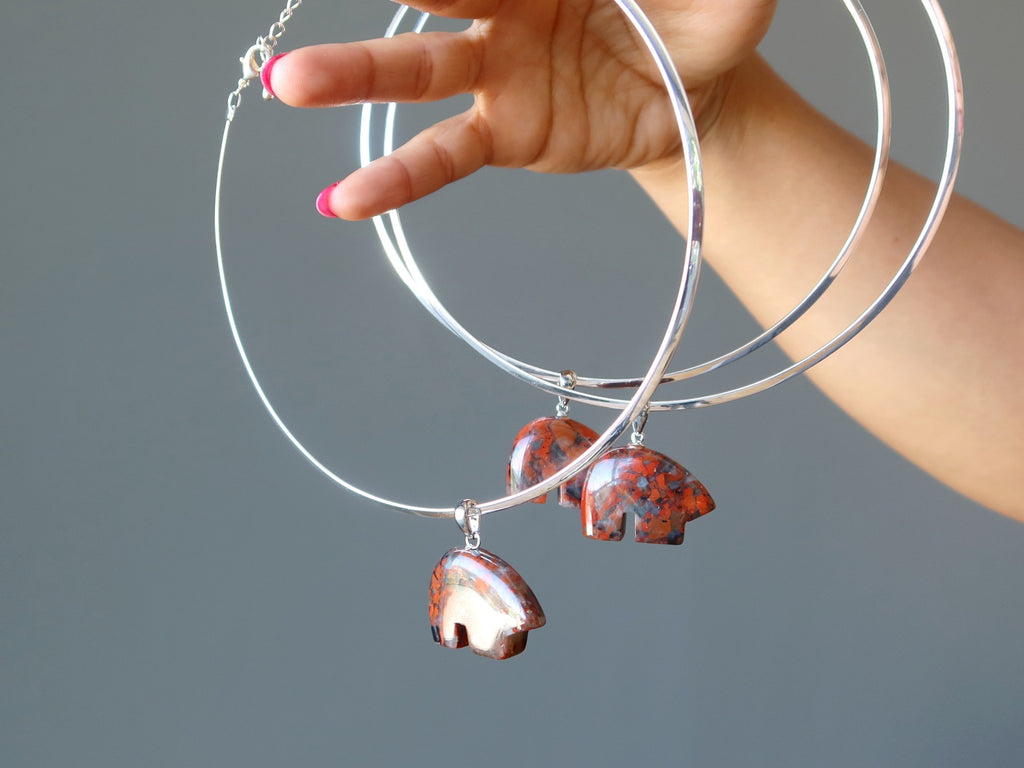 hand holding three silver chokers hanging with red jasper bear pendants