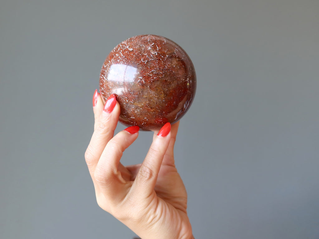 hand holding red quartz sphere