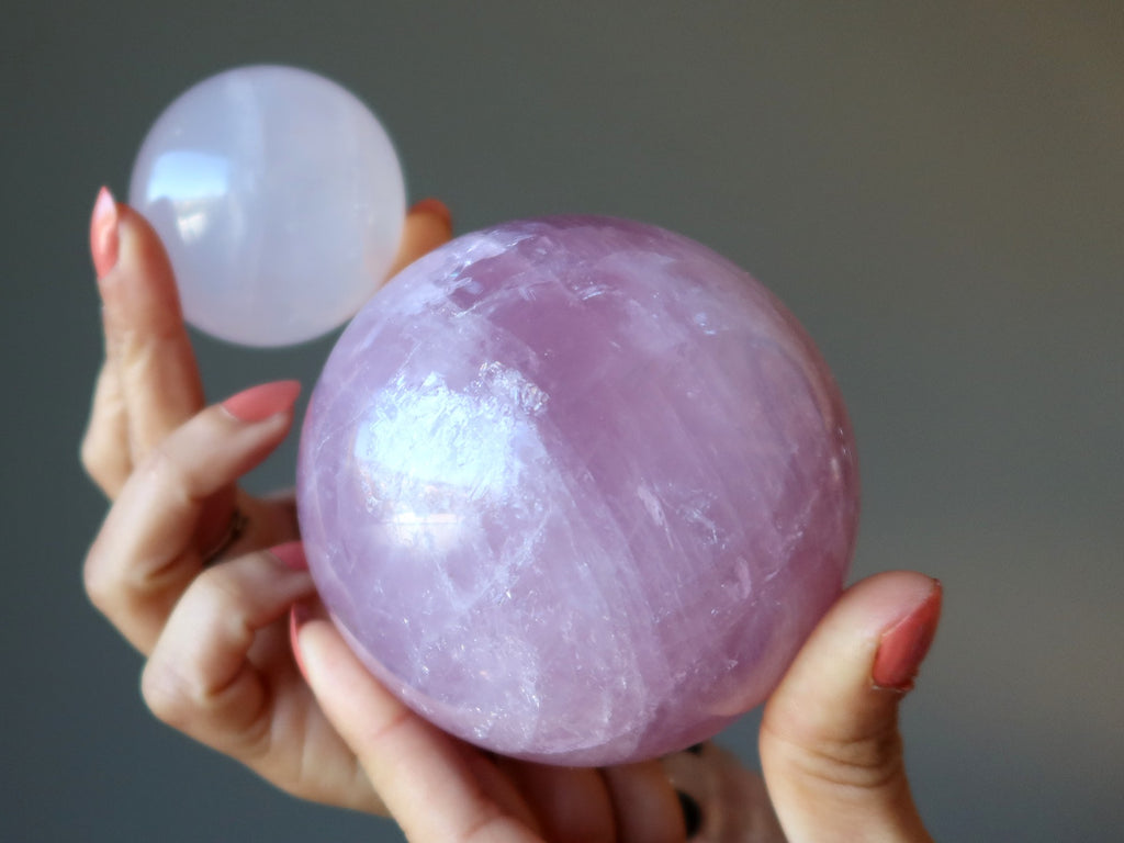hands holding up a pale pink and a dark pink rose quartz sphere