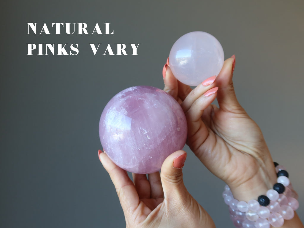 hands holding up a dark pink and a light pink rose quartz sphere to show natural pinks vary