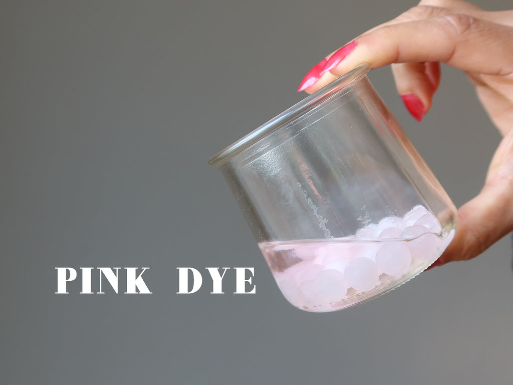 rose quartz beads in a jar showing pink dye seeping into acetone