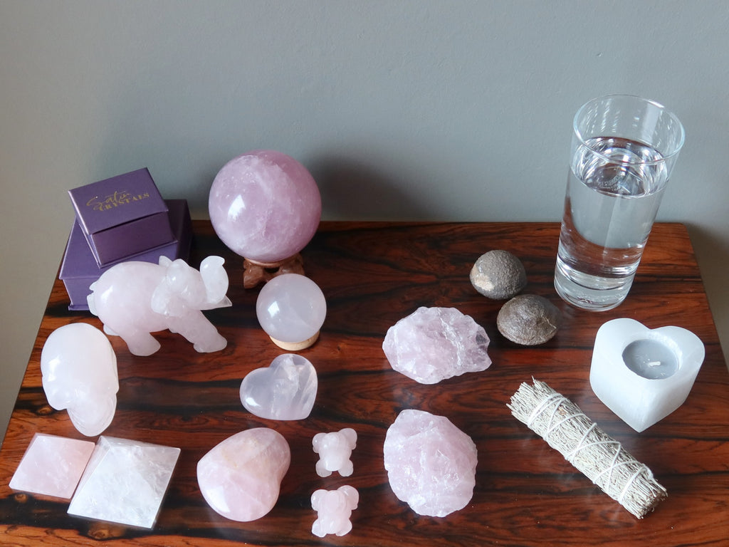 rose quartz crystals, moqui stones, candle, sage, water on a table