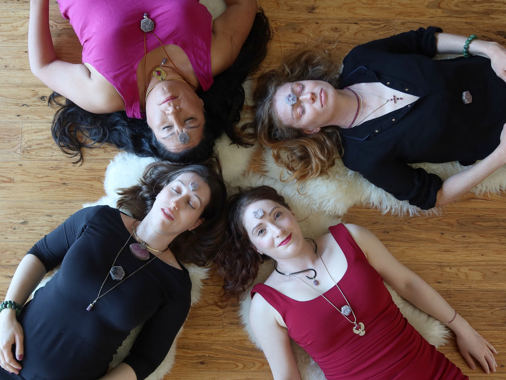 four women lying with ruby crystals in a layout