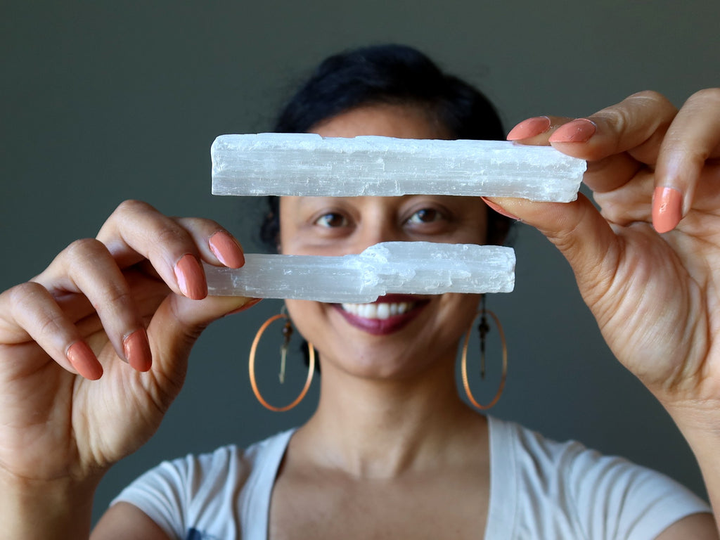 woman holding up two sticks of white selenite satin spar wands