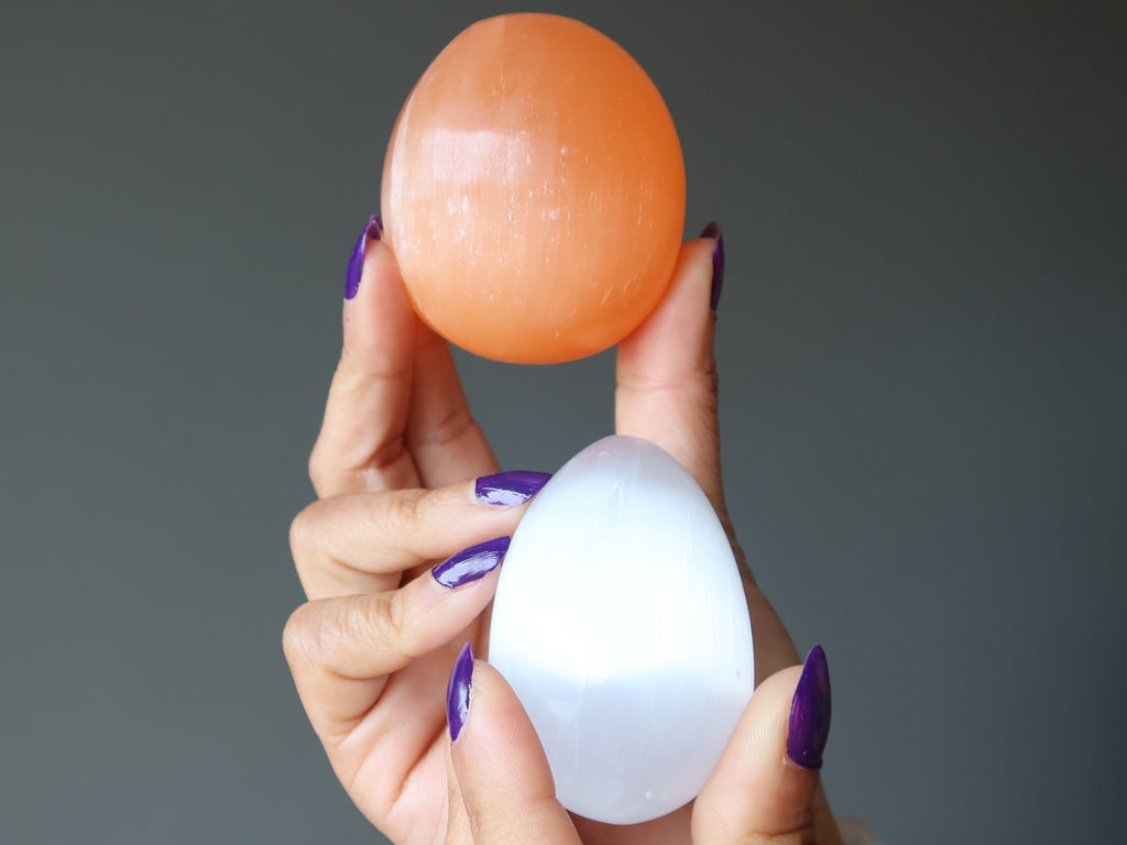 hands holding white and orange selenite eggs