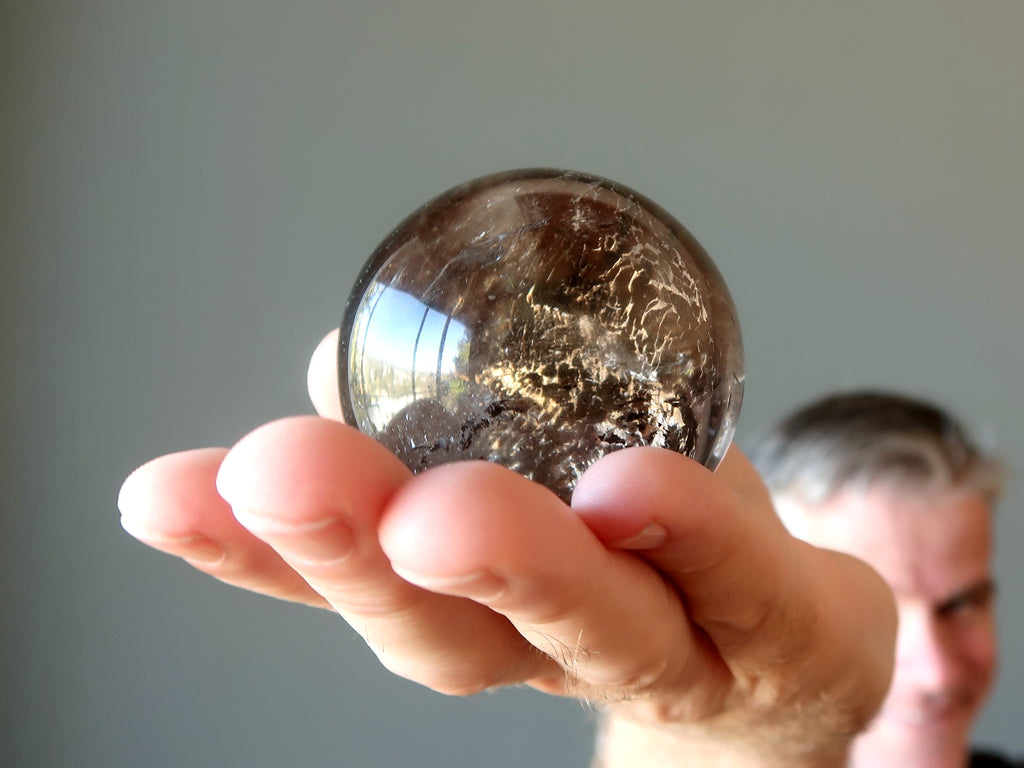 man holding smoky quartz sphere