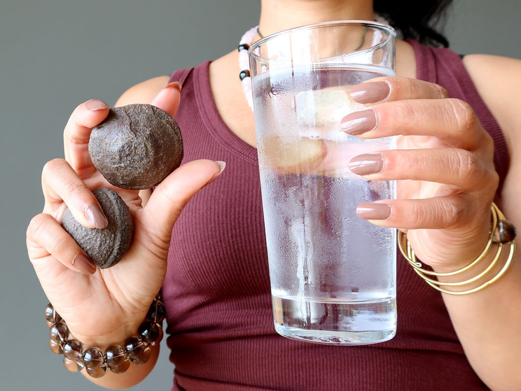 woman holding glass of water and moqui marbles