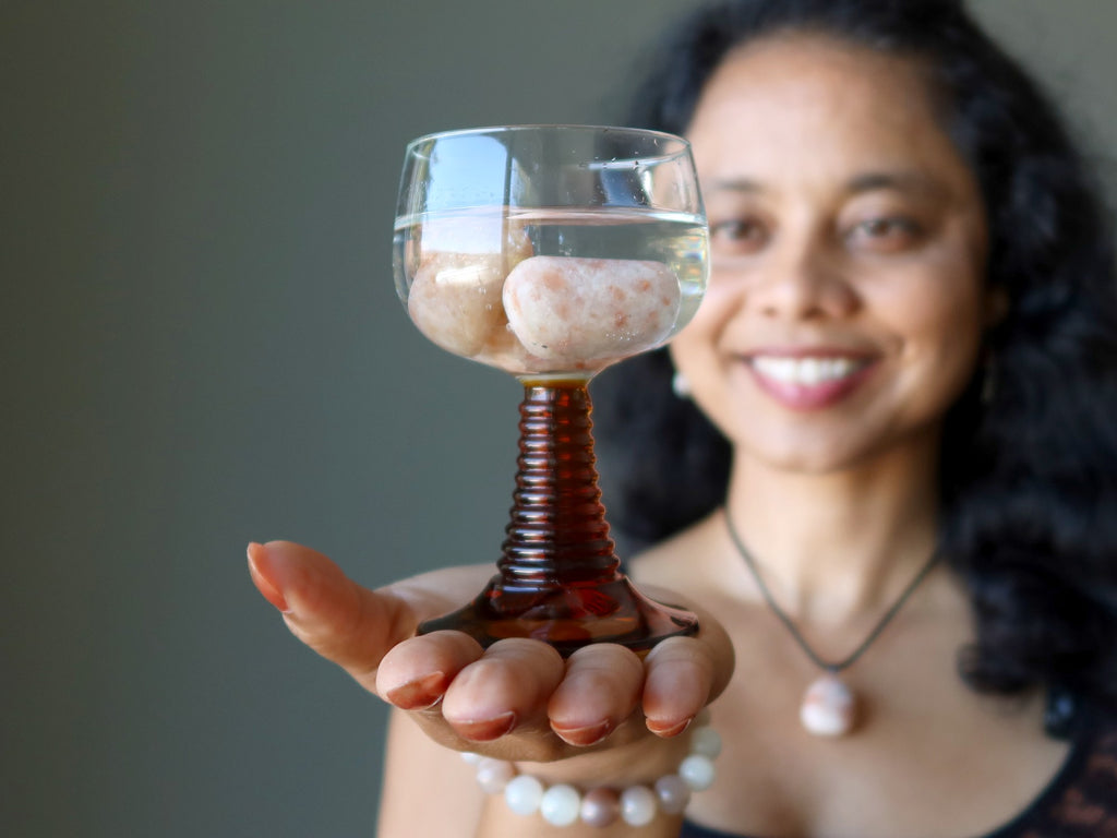 woman holding goblet of sunstone tumbles in water