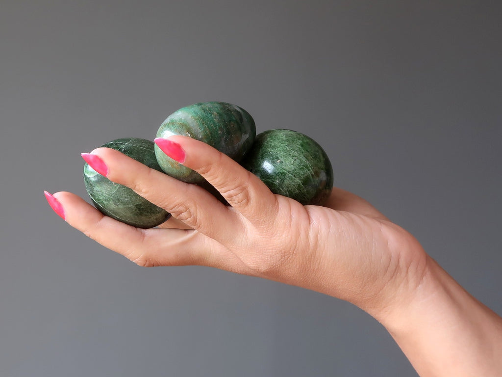 hand holding three green diopside stone eggs