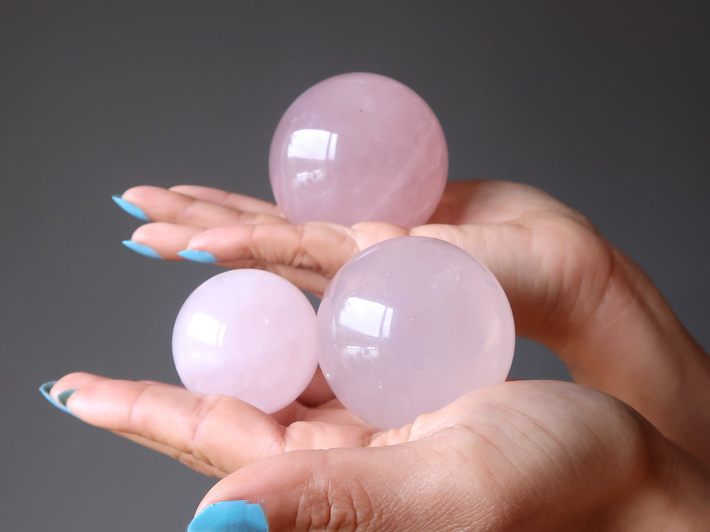 hands holding three rose quartz spheres